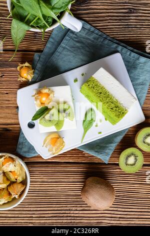 Delizioso pan di Spagna di spinaci condito con cagliata mescolata con panna montata, decorato con frutti di bosco dorati e fette di kiwi Foto Stock
