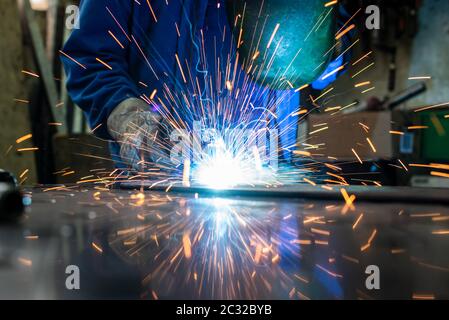 Saldatrice nella sua officina di metallo di saldatura, un sacco di scintille battenti intorno Foto Stock