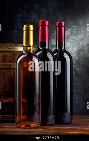 Tre bottiglie di vino vicino al barile di legno in cantina Foto Stock