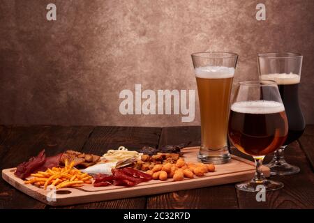 Tre bicchieri con birra diversa e un set di spuntini di vario genere: Jerky, patatine, noci salate, pesce, cracker piccanti di pane, calamari secchi su Foto Stock