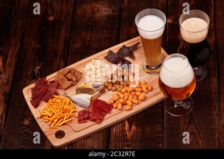 Tre bicchieri con birra diversa e un set di spuntini di vario genere: Jerky, patatine, noci salate, pesce, cracker piccanti di pane, calamari secchi su Foto Stock