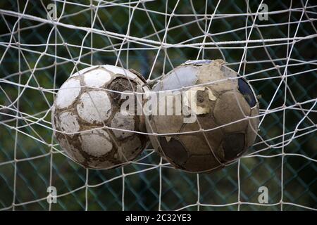 Vista ravvicinata di due vecchie palle di calcio nella rete di obiettivi di calcio. Foto Stock