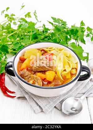 Piatto nazionale dell'Asia centrale Lagman di carne, tagliatelle e verdure in ciotola su un asciugamano, aglio, prezzemolo su sfondo bianco di legno Foto Stock