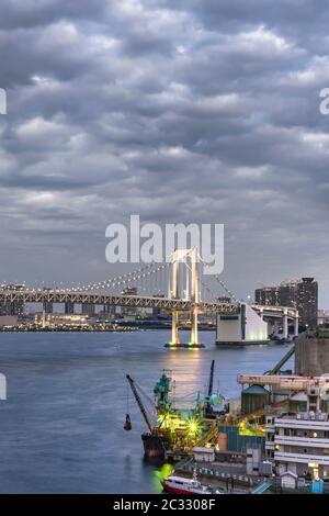 Rainbow Bridge con Cargo e navi da crociera ormeggiate o in barca a vela nella Baia di Odaiba a Tokyo. Foto Stock