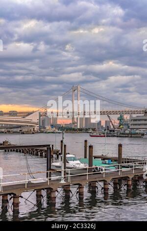 Rainbow Bridge con Cargo e navi da crociera ormeggiate o in barca a vela nella Baia di Odaiba a Tokyo. Foto Stock