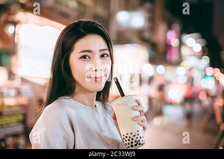 Donna asiatica gustare latte bolla tè con cibo di strada nella notte di mercato Foto Stock