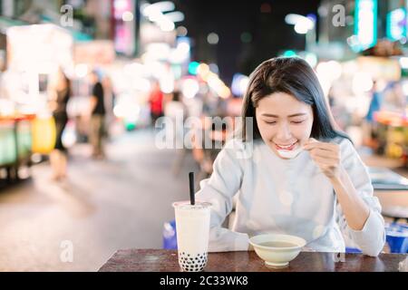 Donna asiatica gustare latte bolla tè con cibo di strada nella notte di mercato Foto Stock