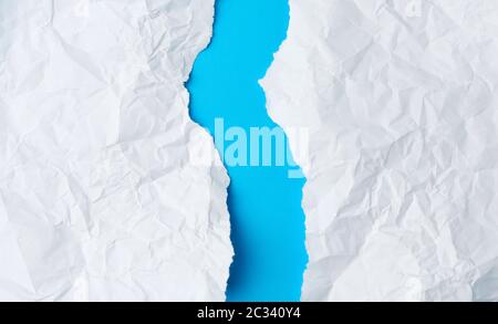 foglio di carta bianco sbriciolato strappato in due su sfondo blu. Bordo strappato del foglio di carta. Foto Stock