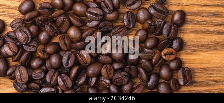 Caffè appena tostato in grani. Sfondo di chicchi di caffè tostati marrone sparsi su un tavolo fatto di tavole di legno. Primo piano. La disposizione della vie superiore Foto Stock