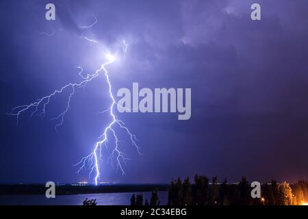 Fulmine nel cielo notturno sopra il fiume Foto Stock