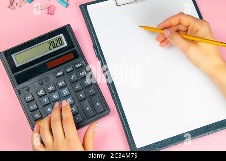 Le mani di una donna contano su una calcolatrice e scrivono note. Vista dall'alto delle mani di una donna d'affari su un foglio bianco. Concetto di finanza e business. Foto Stock
