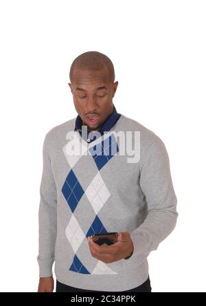 Un giovane arrabbiato americano africano uomo in piedi in un maglione con il suo telefono cellulare in mano confuso ciò che vede, isolato per sfondo bianco Foto Stock