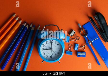 Matite, orologio con allarme blu, bussola, righello e pinzatrice su sfondo arancione. Foto Stock