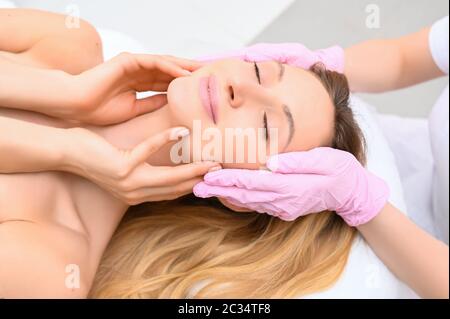 Closeup di mani estetiste in guanti che toccano il viso della giovane donna. Concetto di chirurgia plastica. Bellezza del viso. Foto Stock