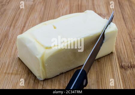 Mantello rettangolare di burro con coltello nero su fondo di legno Foto Stock