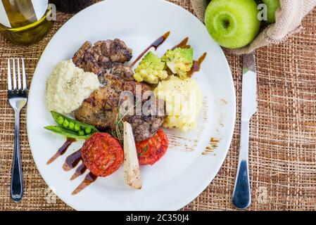 bistecche in salvia e salsa di mele servite con verdure. fette di manzo arrosto con salsa di frutti di bosco, mela e pera, patate e insalata verde Foto Stock