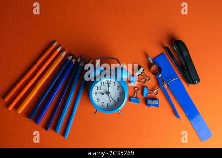 Matite, orologio con allarme blu, bussola, righello e pinzatrice su sfondo arancione. Foto Stock