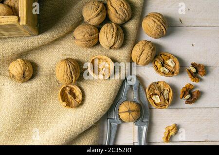 Noci in una scatola di legno, che si trova su un vecchio sacco rustico, anche sparso su un tavolo bianco nelle vicinanze è un cracker di noce. Foto Stock