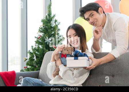 L'uomo bello sta dando alla sua ragazza un regalo di Capodanno. Entrambi sorridono felici l'uno all'altro. sono asiatici Foto Stock