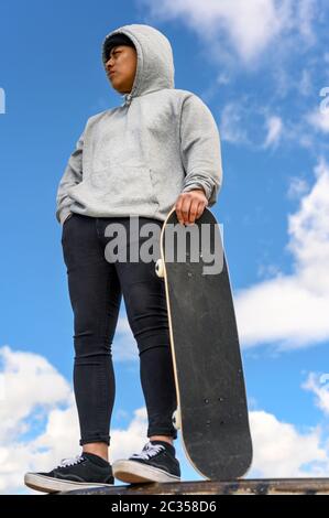 Giovane latino uomo skateboarding di fronte al cielo blu . Foto Stock