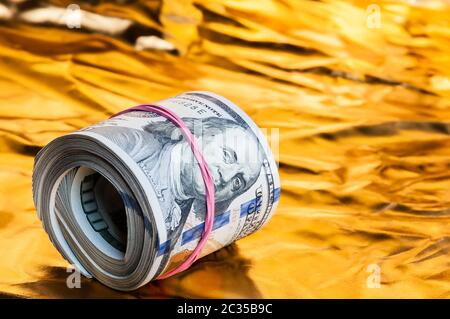 Un rotolo di dollari giace su un fondo dorato Foto Stock