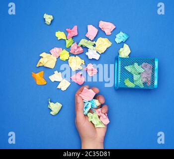 Mano femmina trattiene un mazzetto di accartocciata multi-colore di pezzi di carta, accanto a un metallo spazzatura, Foto Stock