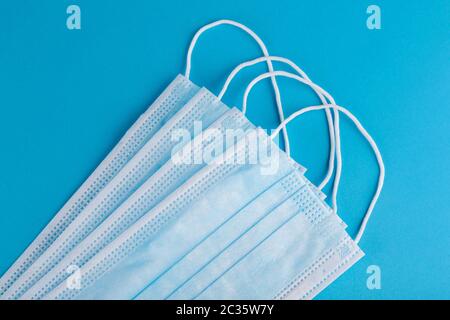 Molte maschere mediche su sfondo blu, primo piano. Maschera chirurgica protettiva. Maschere facciali vista dall'alto, disposizione piatta Foto Stock