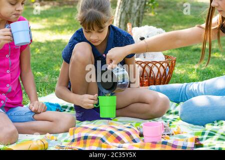 Ad un picnic, una ragazza versa il tè in bicchieri per bambini Foto Stock