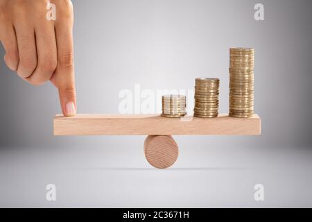 Close-up di una persona del dito impilati di bilanciamento di monete d'oro su altalena in legno Foto Stock