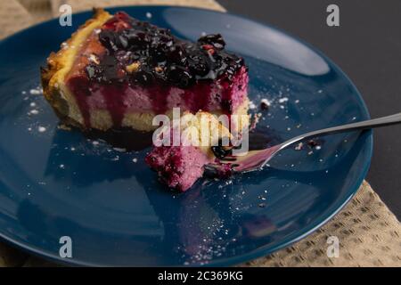 Fette di torta mousse di mirtillo con riflessi frutti di bosco decorati e foglie di menta su una piastra blu sono su tavola nera, primo piano. Viste dall'alto. Foto Stock