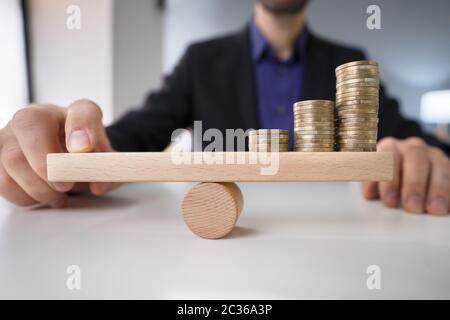 Close-up di un imprenditore la mano di bilanciamento delle monete impilate su altalena in legno con il dito sulla scrivania Foto Stock