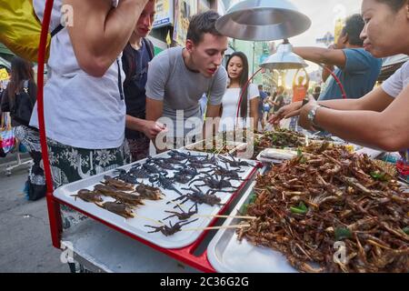 Un turista occidentale sconvolto spider, tarantulas, scorpioni e insetti in vendita in una stalla di cibo a Khao San Rd., Banglamphoo, Bangkok, Thailandia Foto Stock