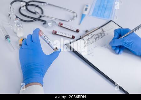 Analyst Hands con guanti protettivi in possesso di COVID 19 Coronavirus test Blood prendendo appunti statistici. Test antivirus e concetto di ricerca. Primo piano Foto Stock