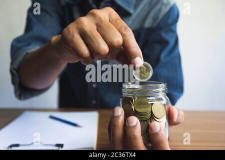 Caduta di mano una moneta in un barattolo di vetro per il business. Finanziari e concetto di contabilità. Foto Stock