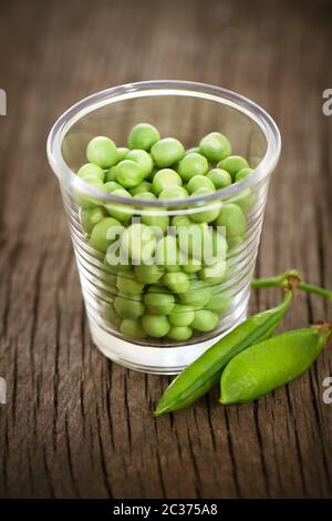 Piselli verdi freschi in piccolo bicchiere sul tavolo rustico Foto Stock