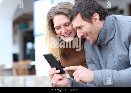 Coppia felice di adulti il controllo smart phone il contenuto online di strada in inverno Foto Stock
