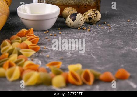 Pasta Conchiglie Rigate, miscela di colorati conchiglie non cotte con dondolo per l'impasto, l'olio d'oliva, spezie e uova di quaglia. Fondo di cibo italiano testurizzato co Foto Stock