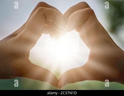 Womans mani cattura la luce solare sunray mentre messa a forma di cuore Foto Stock