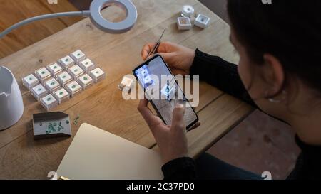 Gemologa che lavora scattando le foto delle pietre smeraldo preziose con il suo telefono mobile. Spazio di lavoro. Foto Stock