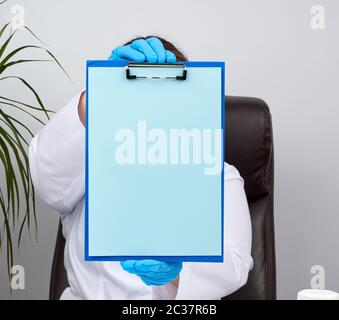 mani del medico in guanti blu in lattice medico tiene una cartella con una graffetta, luogo per la scrittura di una diagnosi, messaggio Foto Stock