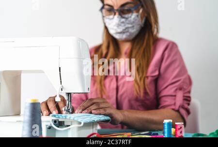 Donna matura che lavora con macchina da cucire facendo maschera medica casalinga per prevenire e fermare la diffusione del virus corona Foto Stock