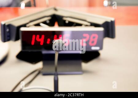 un microfono da tavolo sul tavolo di legno di una tavola davanti a un orologio digitale con cifre rosse. Foto Stock