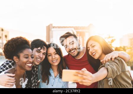 Gruppo amici multirazziali che prendono selfie con smartphone mobile all'aperto - felici persone di razza mista divertirsi all'aperto Foto Stock