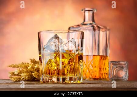 Il whiskey con ghiaccio e spighe di grano su sfondo arancione Foto Stock