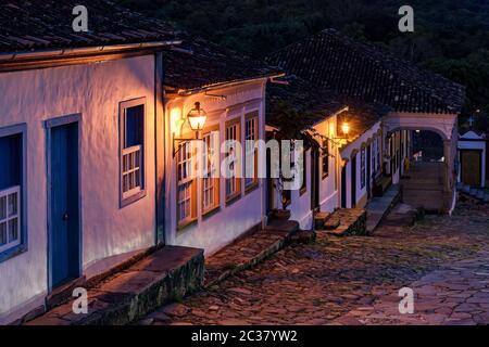 Vista notturna di una vecchia strada acciottolata e delle sue case in stile coloniale illuminate da lanterne a Tiradentes Foto Stock