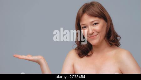 Bella donna sorridente pubblicizza nuovo prodotto. Donna caucasica dai capelli rossi mostra la sua mano presentando spazio vuoto per il testo. Concetto di pubblicità Foto Stock