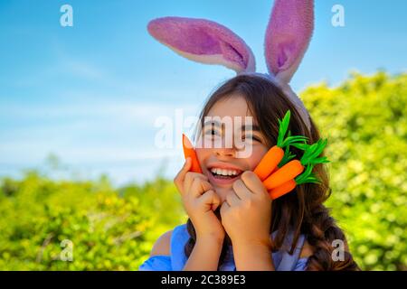 Ritratto di una ragazza carina coniglietto con carote in mani godendo di Pasqua, avendo divertente giardinaggio nel cortile in una giornata di sole primavera, vestito tradizionale Foto Stock