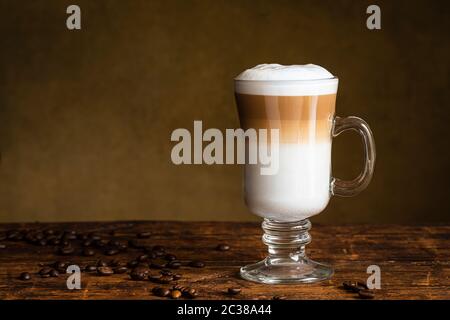 Caffè latte macchiato in un bicchiere di caffè irlandese. La tazza si trova su un tavolo di legno con i chicchi di caffè sul tavolo accanto a. Foto Stock