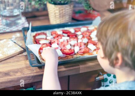 Ragazzo aiuto cucina a casa in cucina. Bambino preparare la pizza con le mani di un bambino e ingredienti freschi come mozzarella, pomodoro e pasta come Foto Stock
