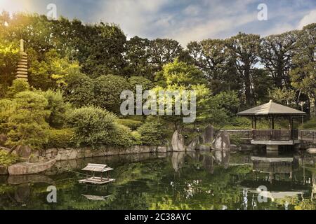 Tramonto su Gazebo esagonale Ukimido nel laghetto centrale del Giardino di Mejiro dove le anatre sono riposanti e. Foto Stock